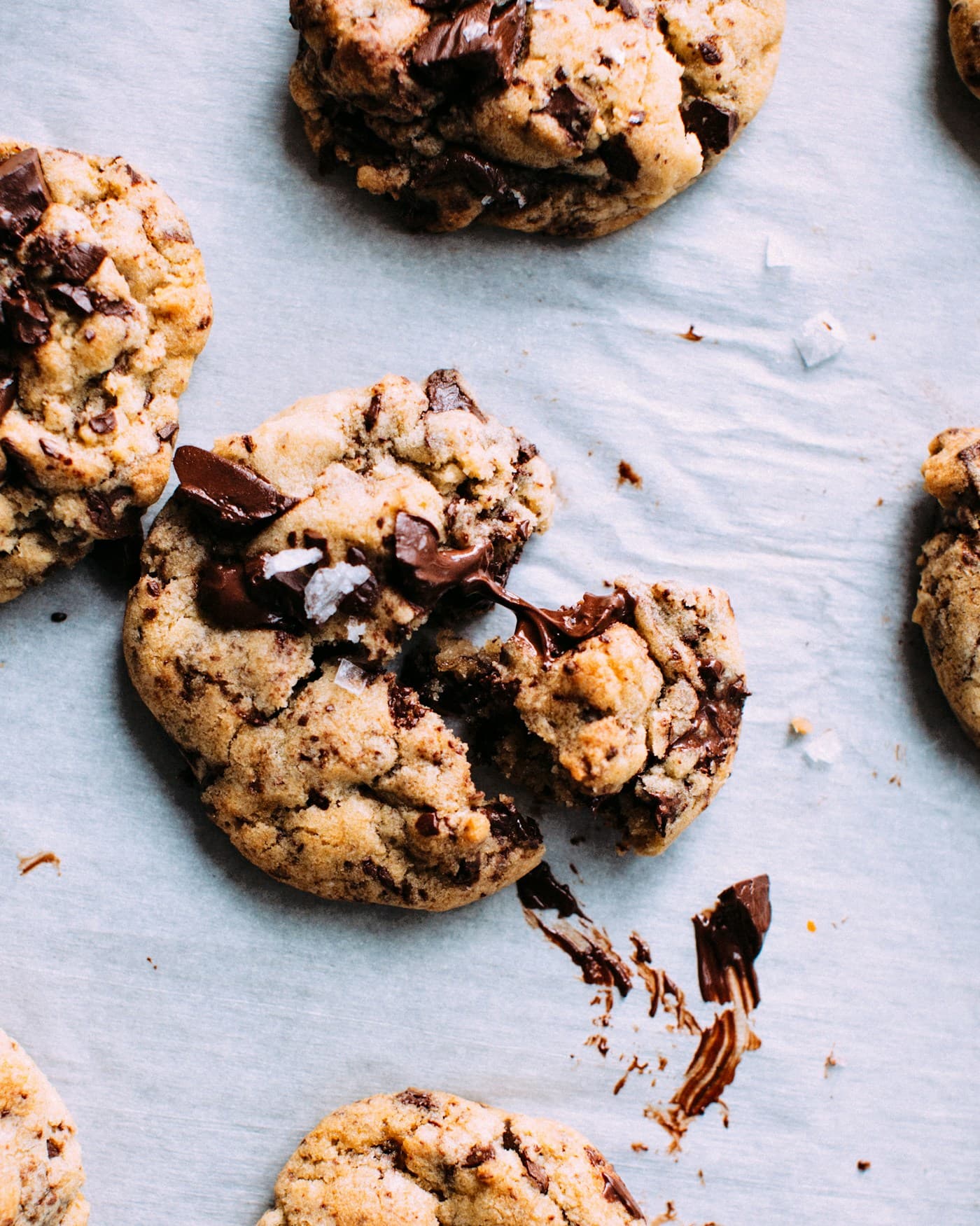 Golden cookies with large dark chocolate pieces and flakes of sea salt on baking paper