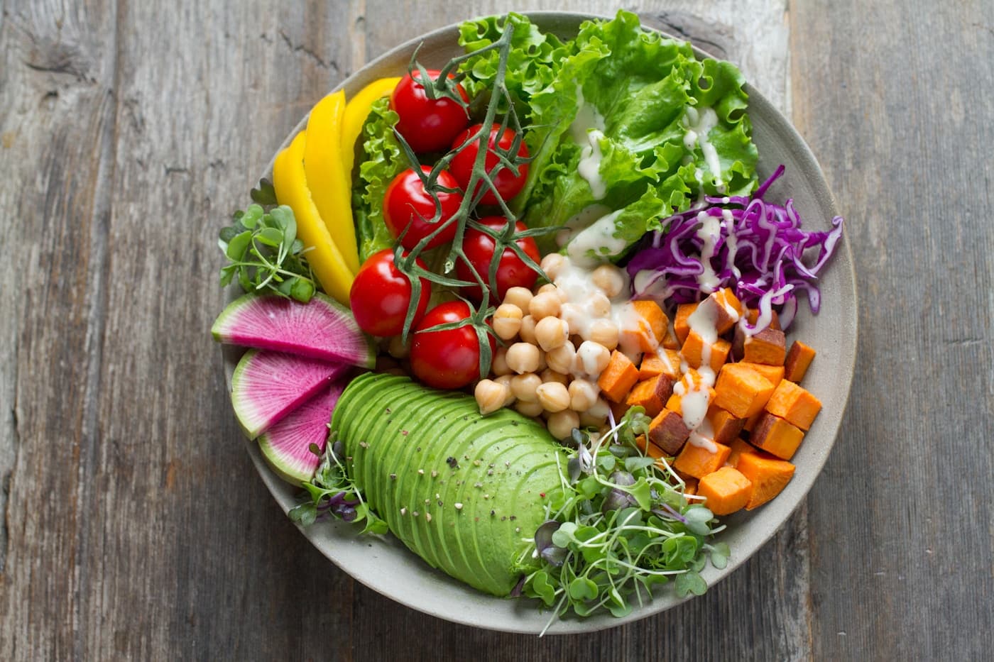 A colourful bowl of avocado, chickpeas, roasted sweet potato, lettuce, tomatoes, cabbage, and radish