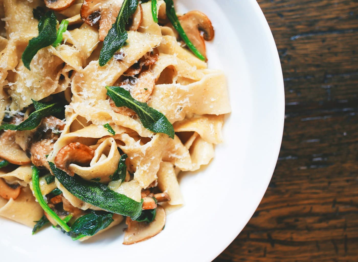 Tagliatelle with golden mushrooms, green sage leaves, and grated Parmesan on a white plate