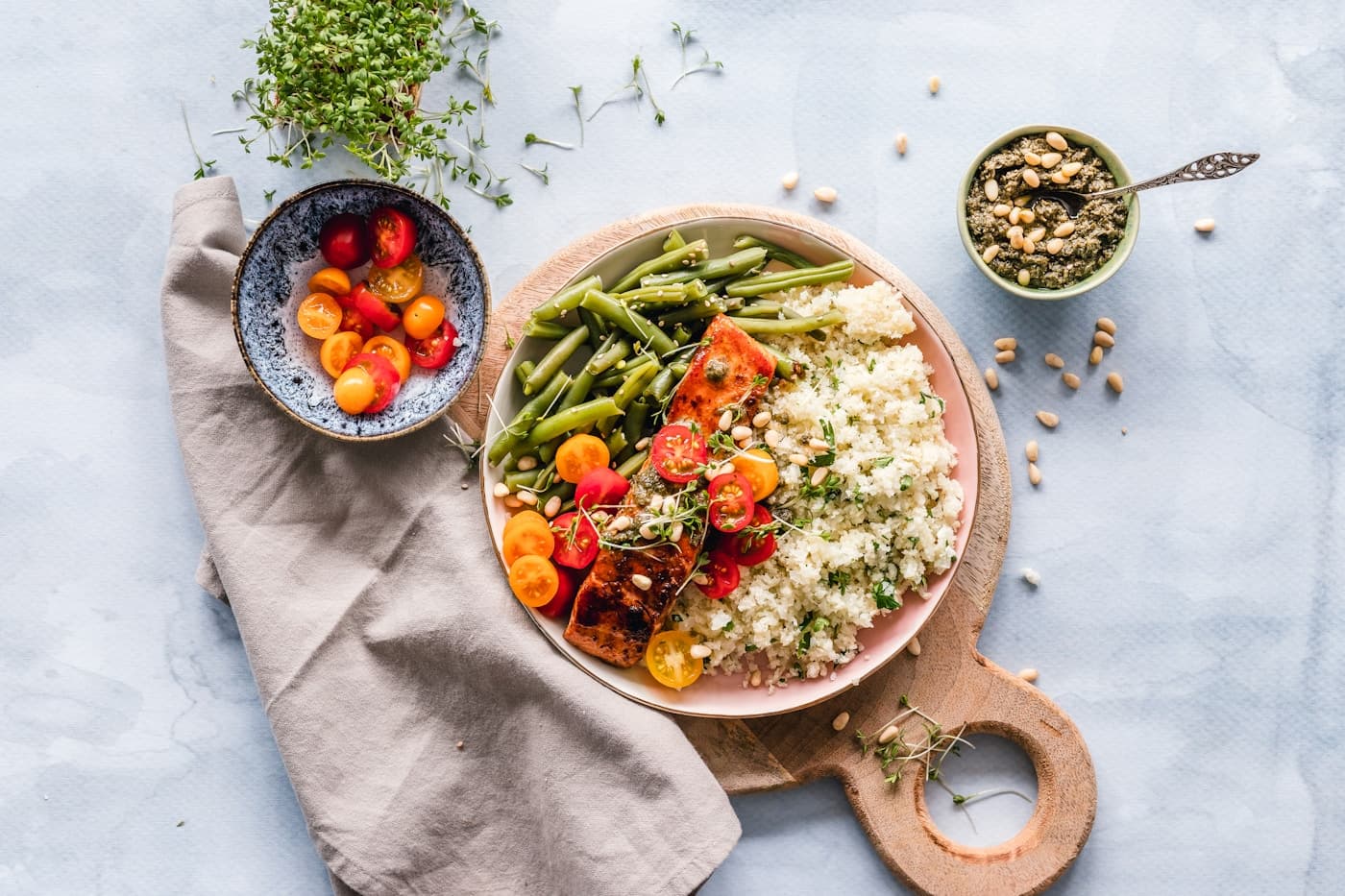 Salmon with couscous, green beans, cherry tomatoes, pesto, and pine nuts on a pink plate
